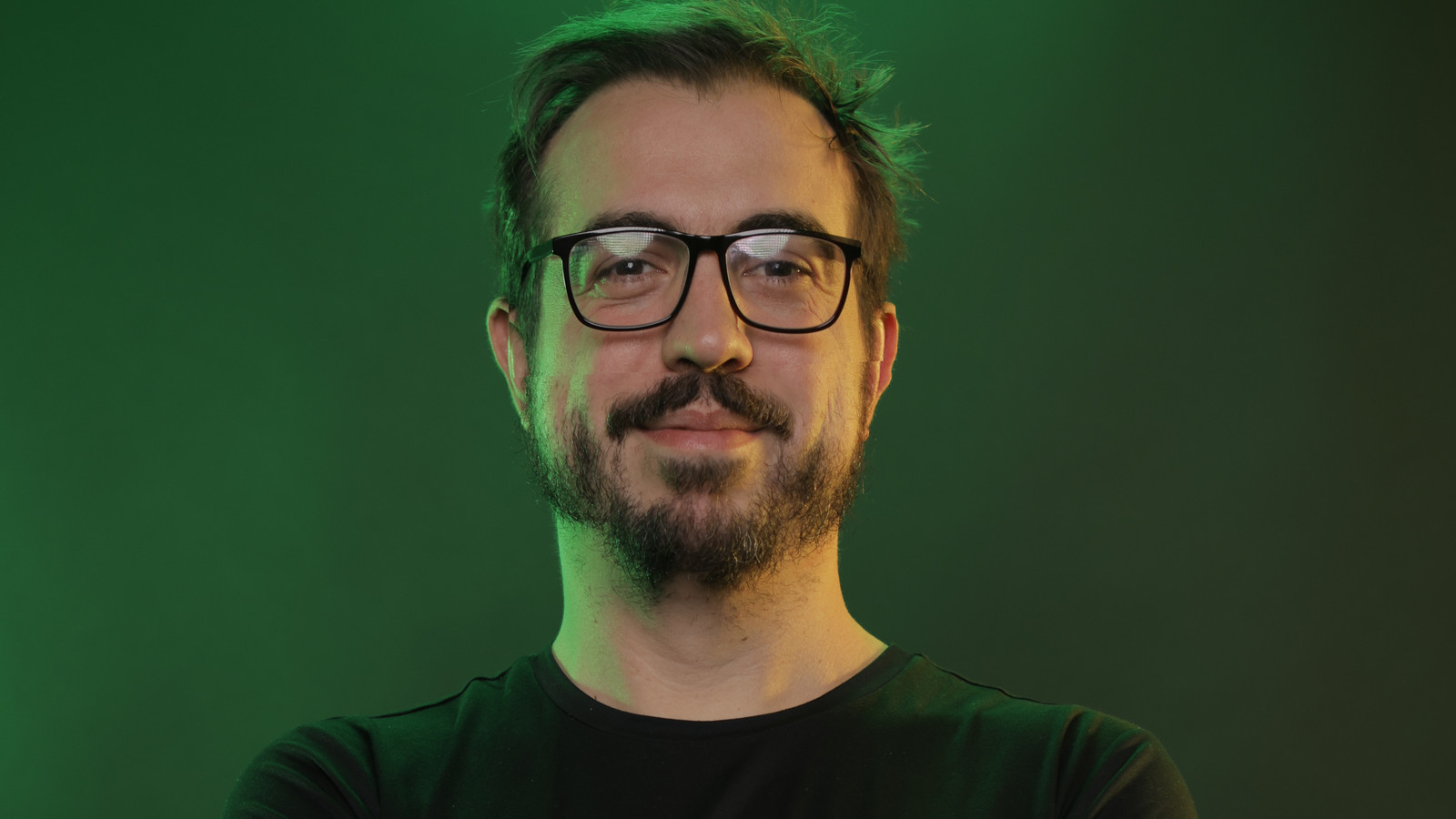 Rafael Artusi, head de produto da CloudWalk, de óculos e camiseta preta, contra fundo verde