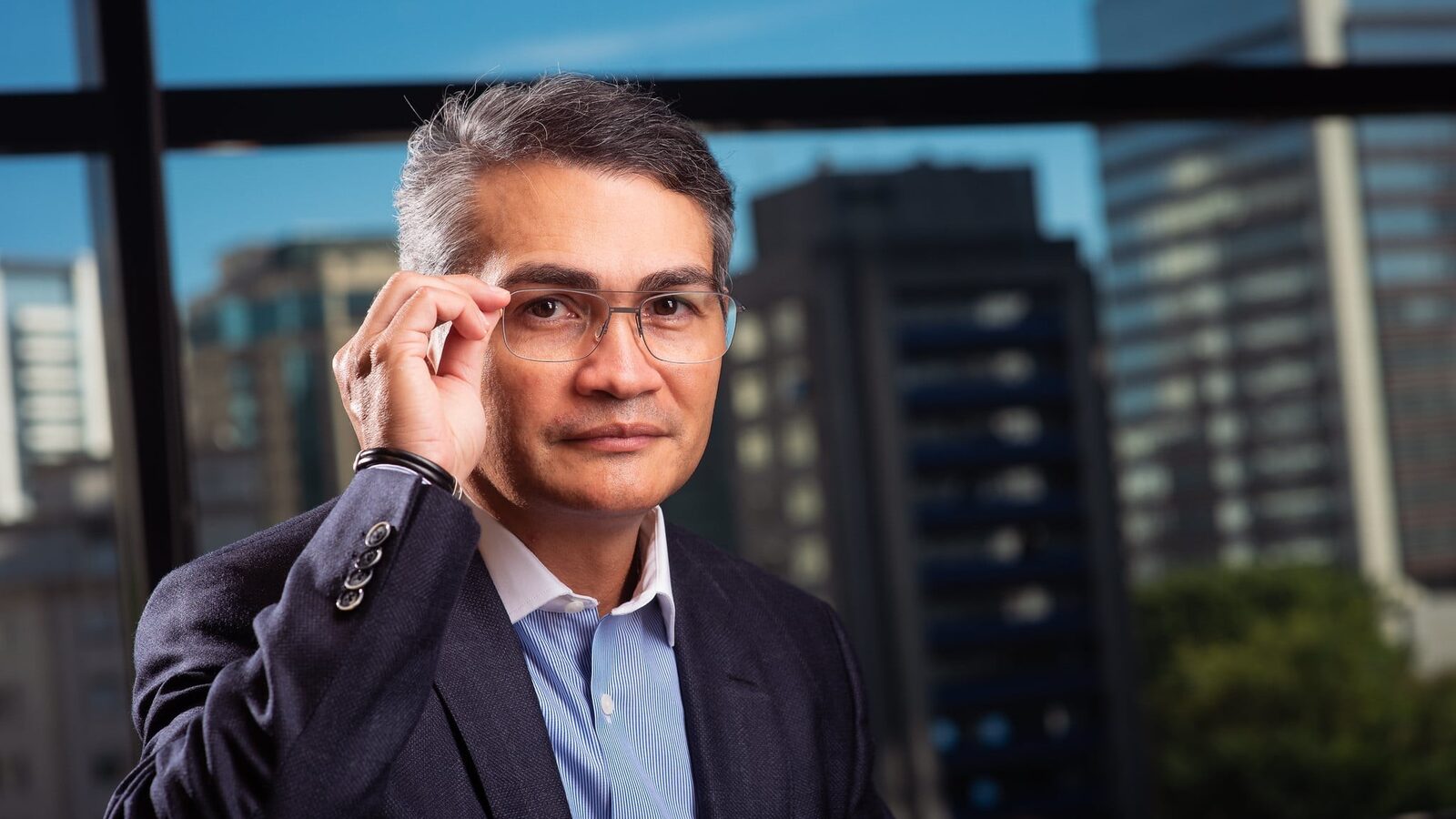 Isaac Sidney, presidente da Febraban, de terno azul e óculos, em retrato com a cidade ao fundo