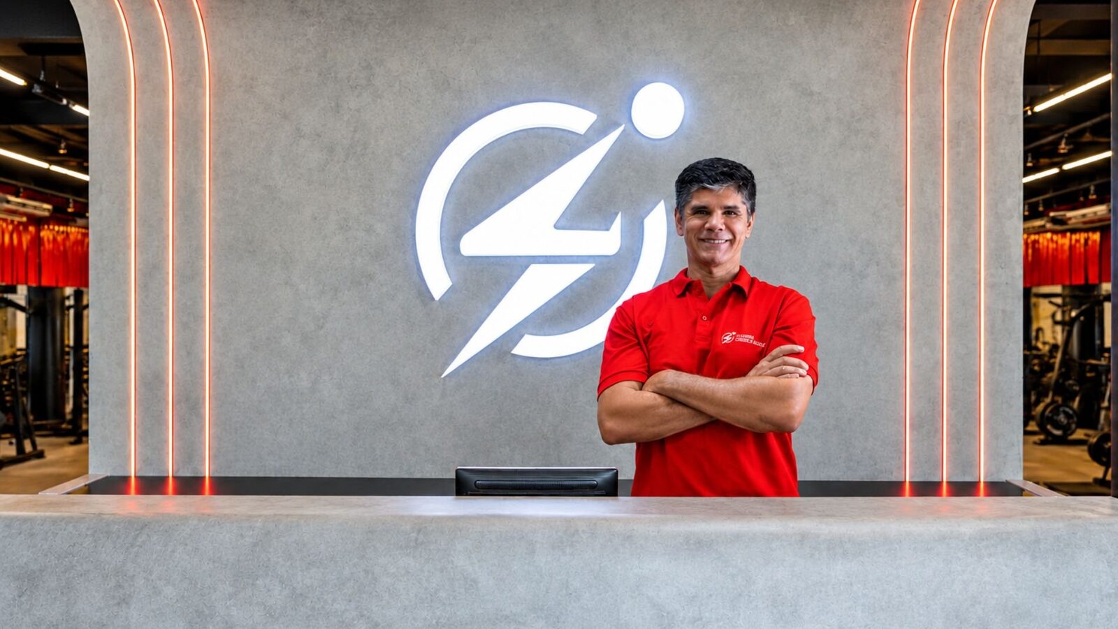 Roberto Oliveira, fundador da Corpo e Saúde, de camisa polo vermelha, de braços cruzados no balcão de uma academia da rede