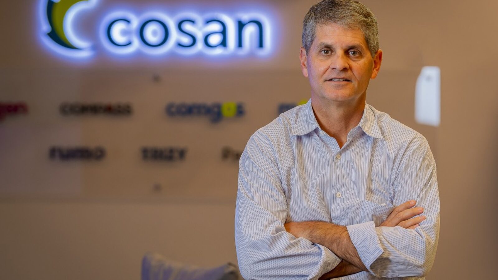 Luis Henrique Guimarães, CEO da Cosan, de paletó escuro, de braços cruzados em frente ao logo da companhia