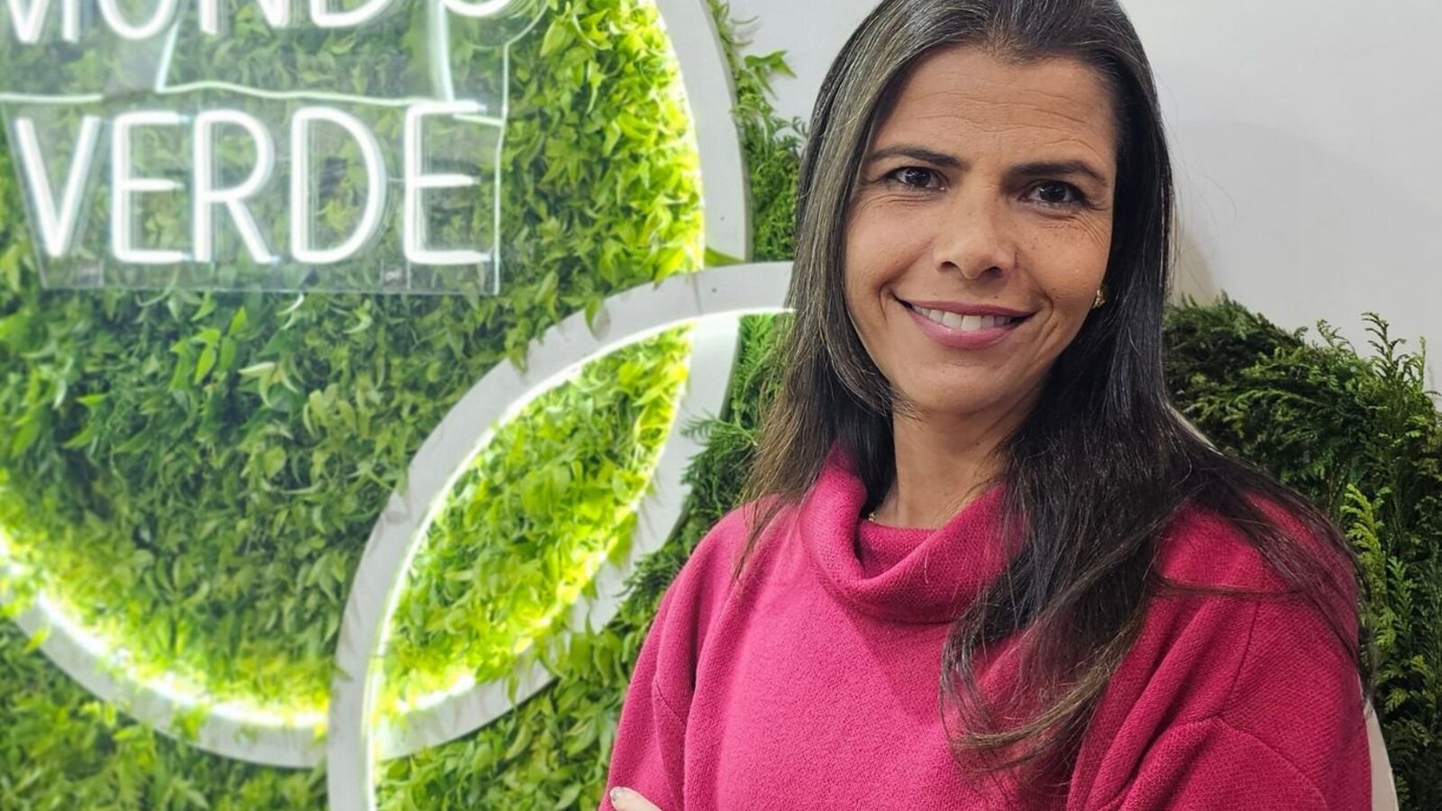 Ana Paula Seixas, CEO da Mundo Verde, de blusa rosa, sorrindo à frente do letreiro da marca