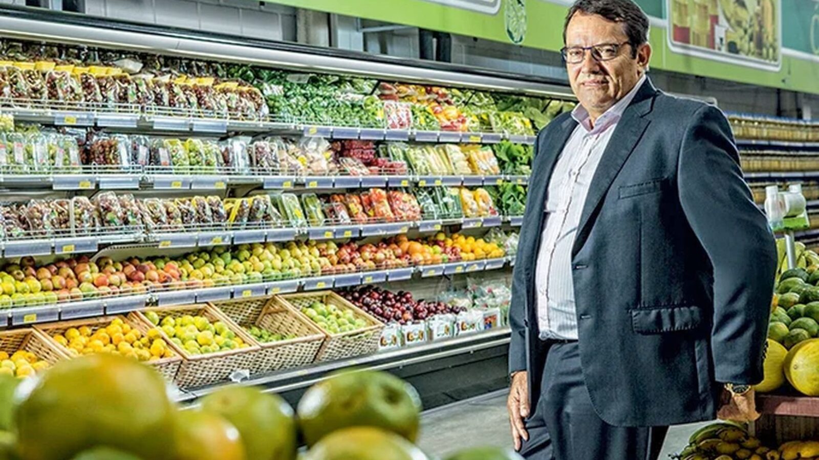 Pedro Lourenço, dono do Supermercados BH, de terno escuro e óculos, em corredor de hortifruti de uma loja da rede