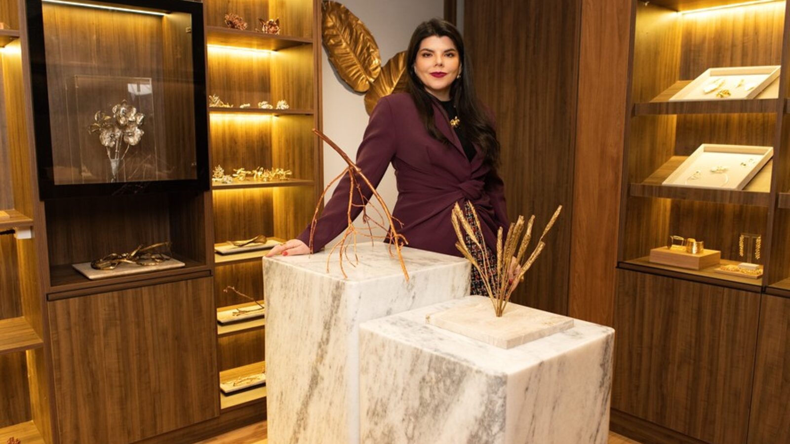 Fernanda Dubeux, CEO da Verde Joias, de blazer vinho, na loja da marca entre vitrines de madeira e pedestais de mármore